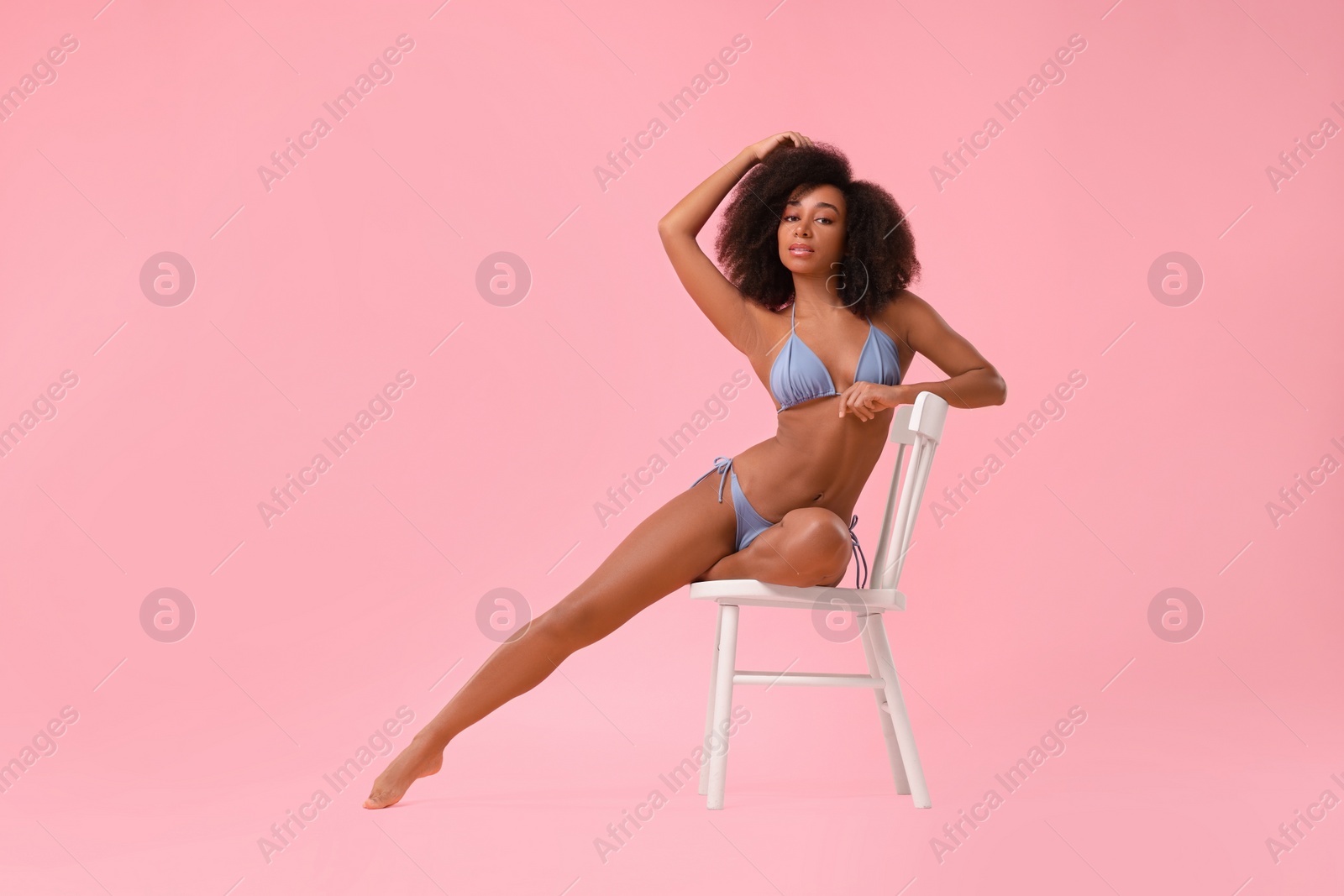 Photo of Beautiful woman in stylish bikini posing on chair against pink background