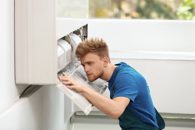 Professional technician maintaining modern air conditioner indoors