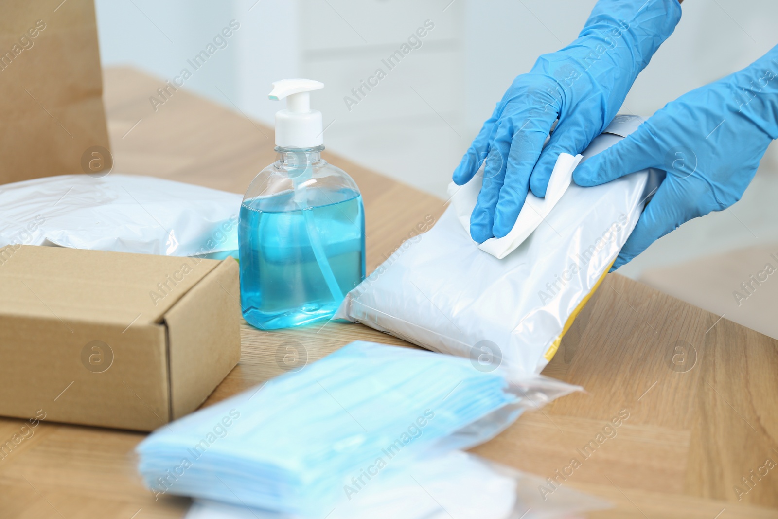 Photo of Woman cleaning parcel with wet wipe at wooden table, closeup. Preventive measure during COVID-19 pandemic