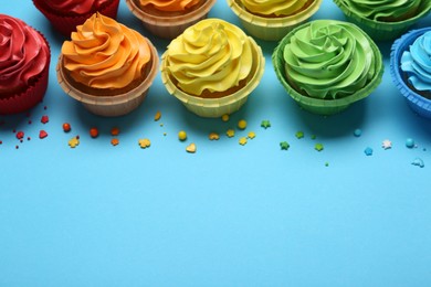 Photo of Many tasty cupcakes with bright cream and sprinkles on light blue background, above view. Space for text