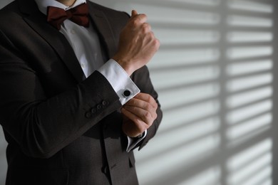 Photo of Man wearing stylish suit and cufflinks near white wall, closeup. Space for text