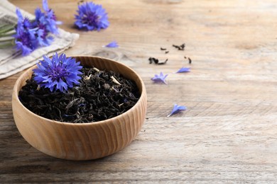 Photo of Dried cornflower tea and fresh flowers on wooden table. Space for text