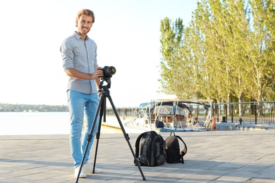 Young male photographer standing with professional camera at pier