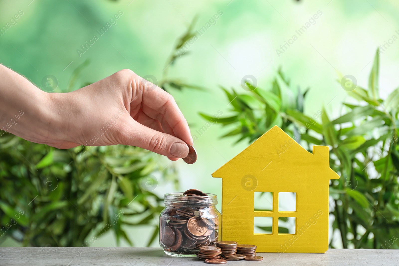 Photo of Woman putting coin into jar near house model on table against blurred background. Space for text