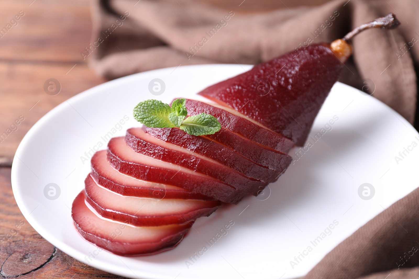 Photo of Tasty red wine poached pear on wooden table, closeup