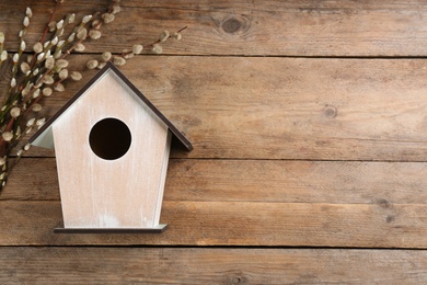 Photo of Beautiful bird house and willow branches on wooden background, flat lay. Spring composition with space for text