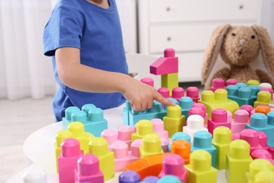 Photo of Little child playing with colorful building blocks at table indoors, closeup