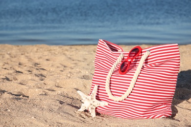Photo of Bag with beach objects on sand near sea. Space for text