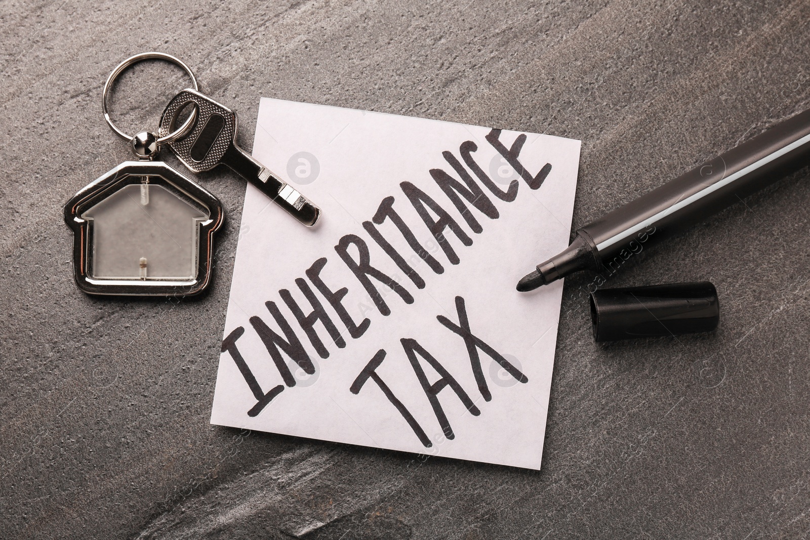 Photo of Inheritance Tax. Paper note, key with key chain in shape of house and marker on grey table, flat lay