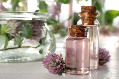 Beautiful clover flowers and bottles of essential oil on white wooden table. Space for text