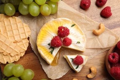 Photo of Brie cheese served with berries and honey on wooden table, flat lay