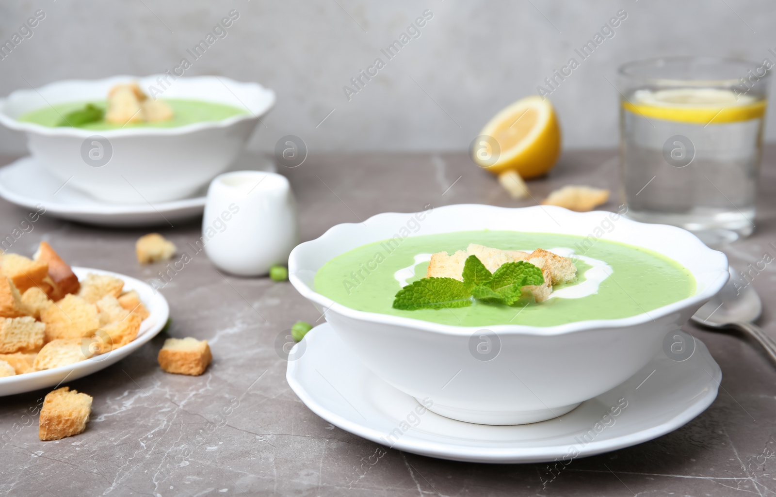 Photo of Green pea soup with croutons in bowl on table