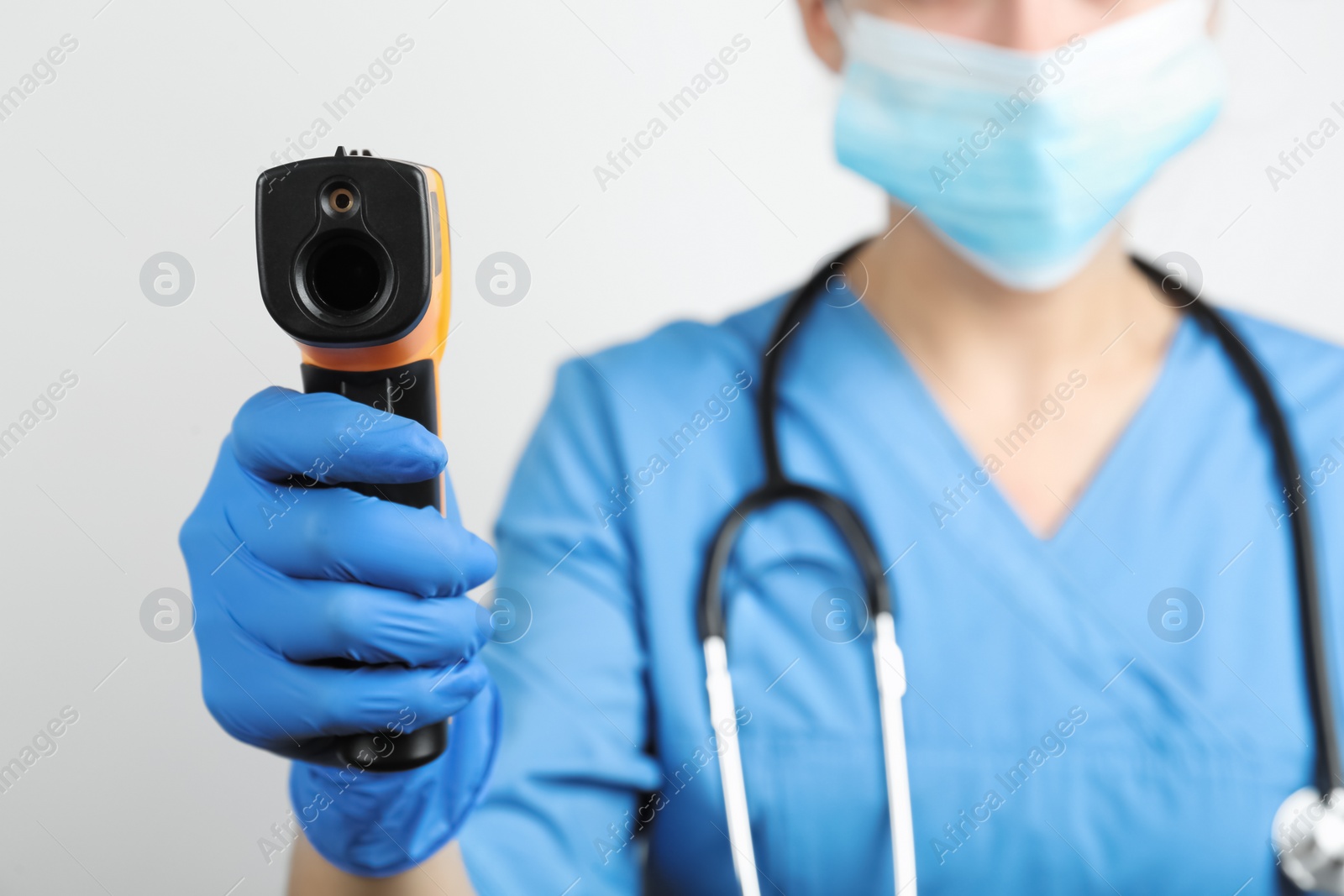Photo of Doctor with infrared thermometer on light background, closeup. Checking temperature during Covid-19 pandemic