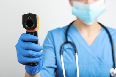 Doctor with infrared thermometer on light background, closeup. Checking temperature during Covid-19 pandemic