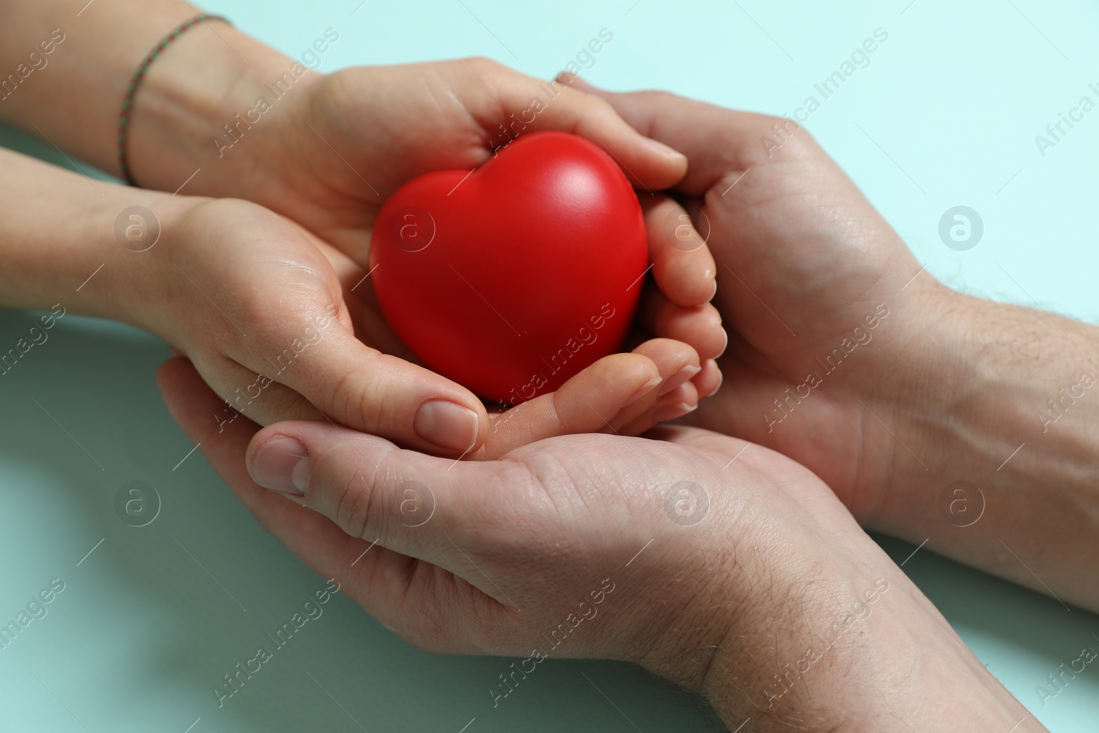 Photo of Couple holding red decorative heart on light blue background, closeup