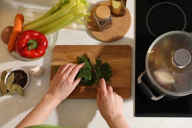 Photo of Woman cutting dill to make bouillon at countertop, top view. Homemade recipe