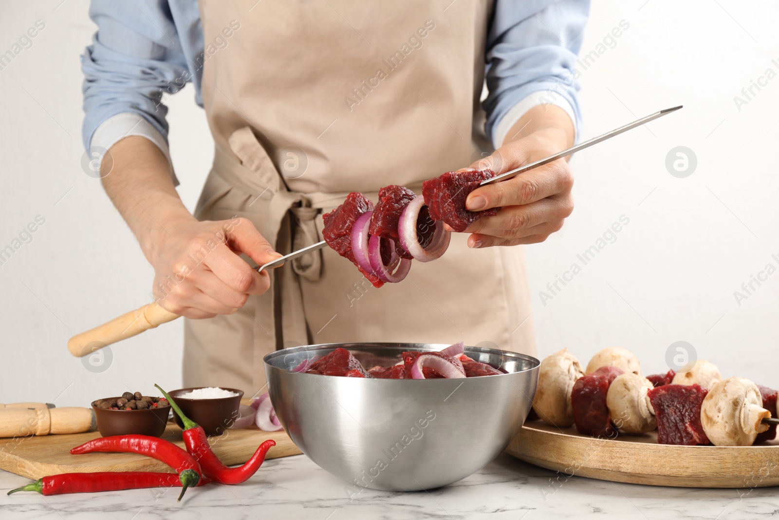 Photo of Woman stringing marinated meat on skewer at white marble table, closeup