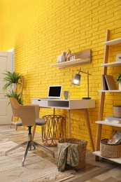 Photo of Modern workplace interior with wooden furniture and laptop near yellow brick wall