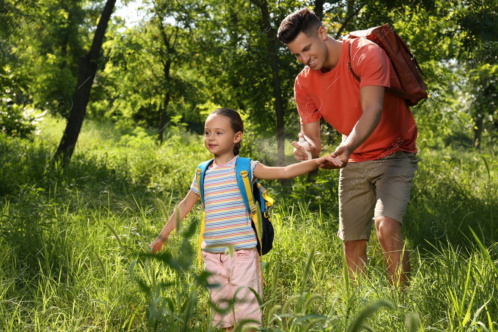 Photo of Father spraying tick repellent on his little daughter's arm during hike in nature