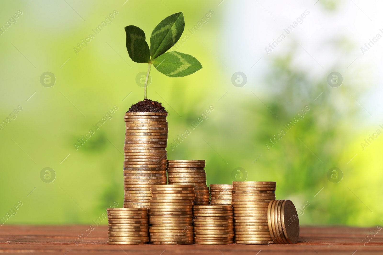 Photo of Stacked coins and green sprout on wooden table against blurred background. Investment concept
