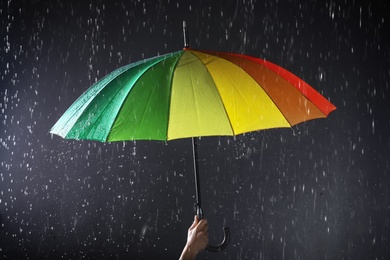 Photo of Woman holding bright umbrella under rain on dark background, closeup