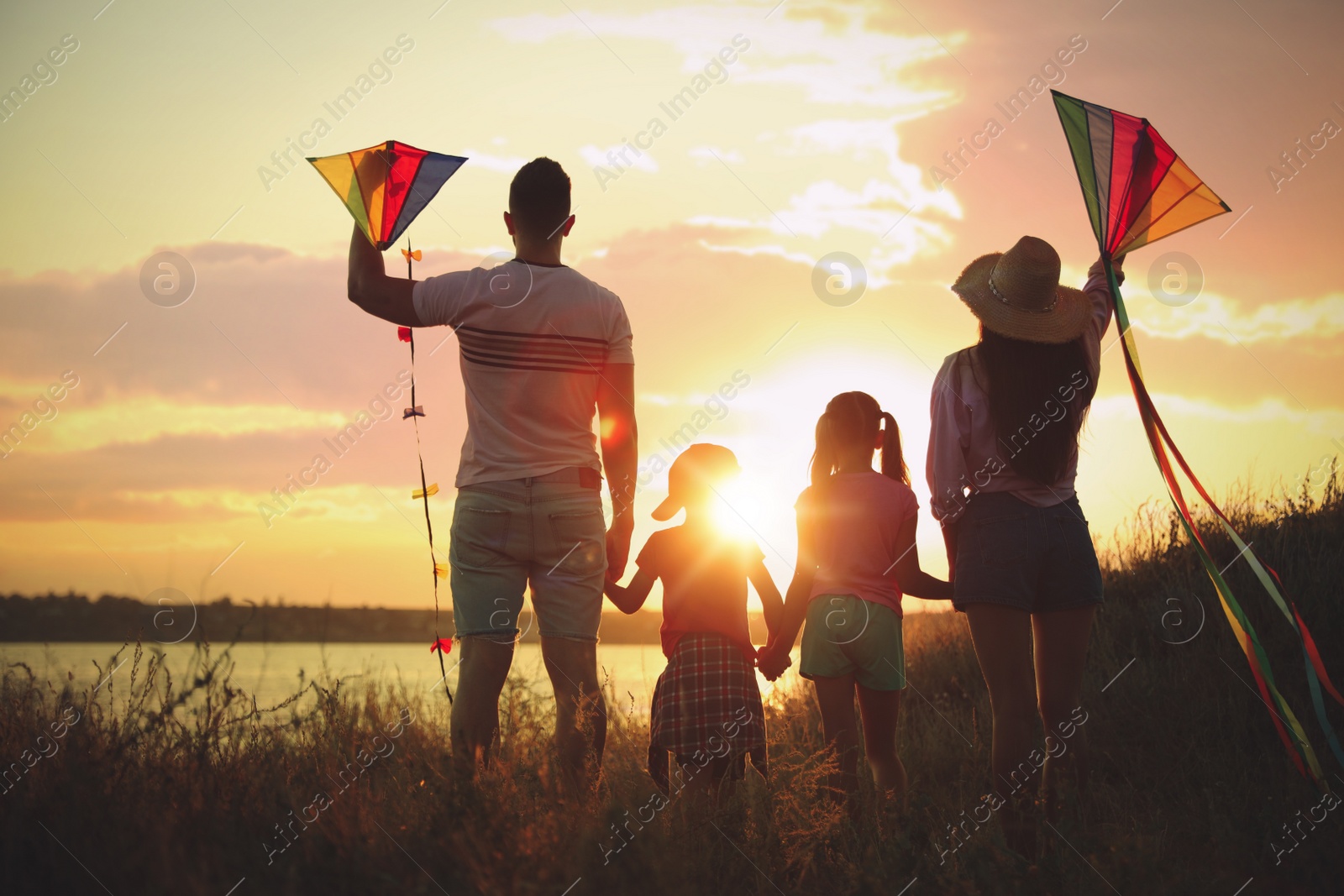 Photo of Parents and their children playing with kites outdoors at sunset, back view. Spending time in nature