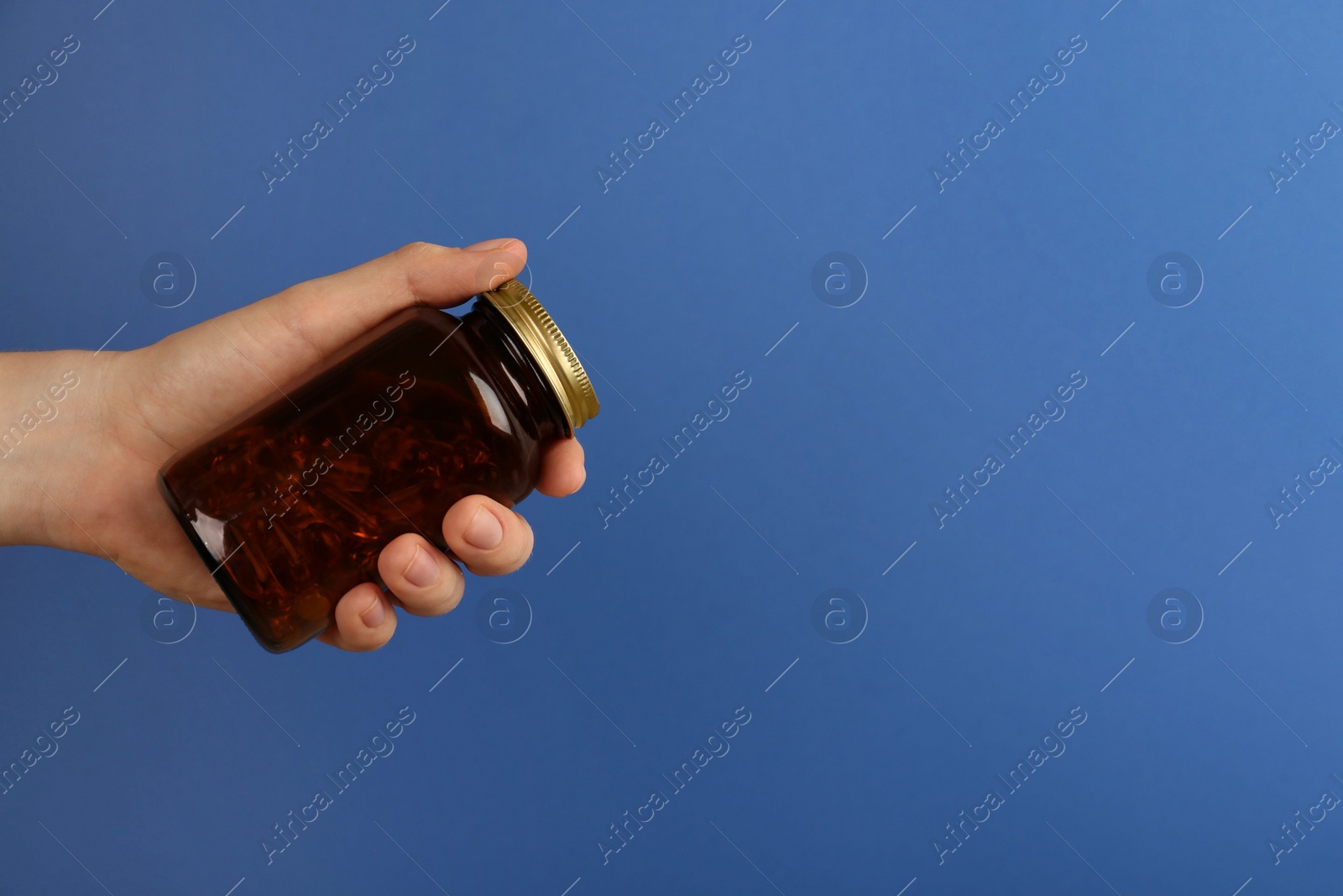 Photo of Woman holding jar with vitamin capsules on blue background, closeup. Space for text