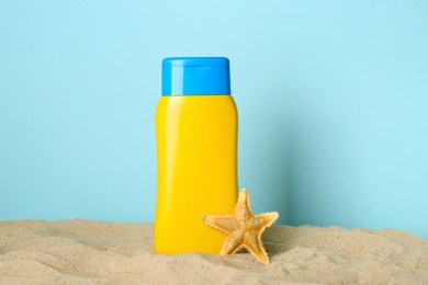 Suntan product and starfish on sand against light blue background