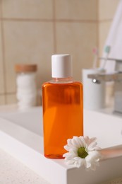 Photo of Fresh mouthwash in bottle and chamomile on sink in bathroom, closeup