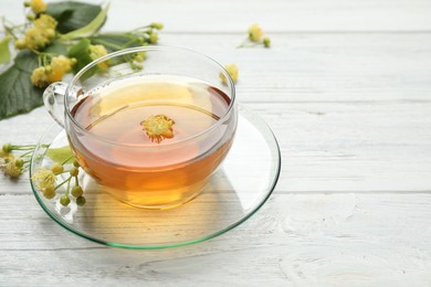 Photo of Cup of tea and linden blossom on white wooden table. Space for text