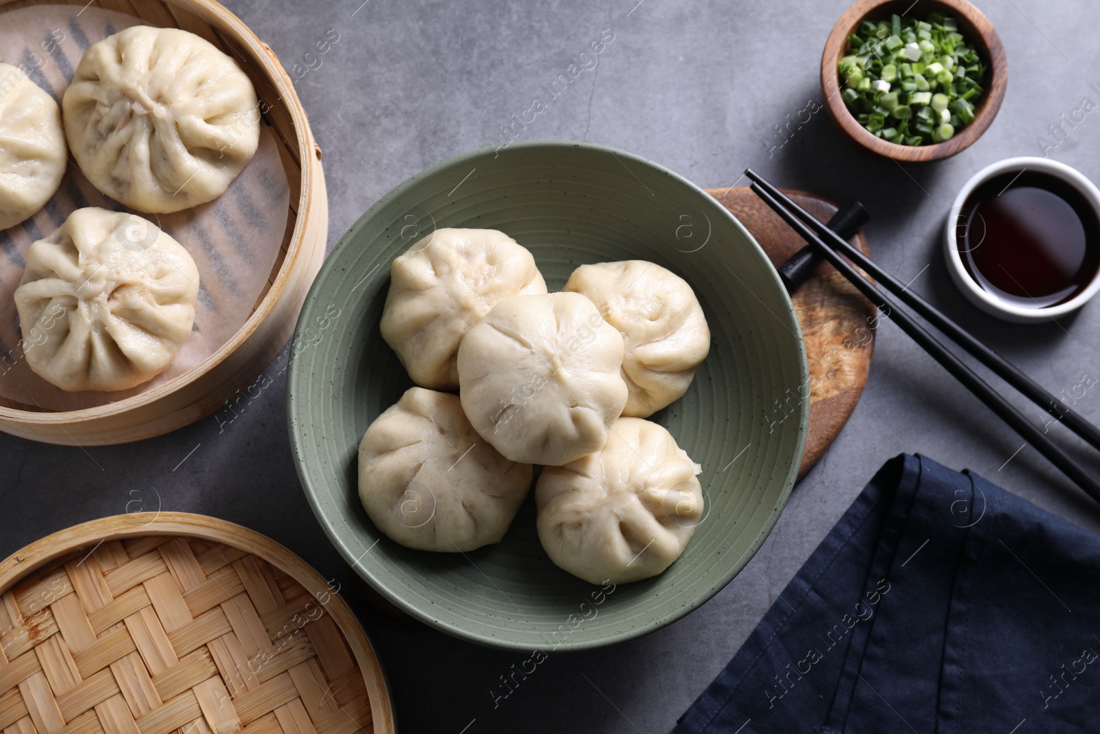 Photo of Delicious bao buns (baozi), chopsticks, soy sauce and green onion on grey table, flat lay