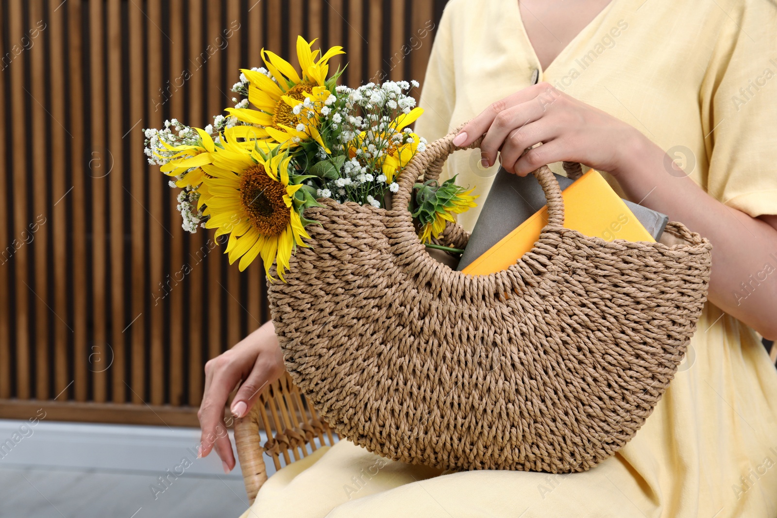 Photo of Woman holding beach bag with beautiful bouquet of flowers and books indoors, closeup