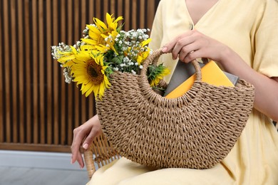 Photo of Woman holding beach bag with beautiful bouquet of flowers and books indoors, closeup