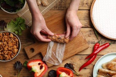 Photo of Woman making tasty spring roll at wooden table, top view