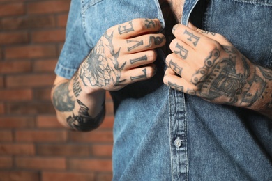 Photo of Young man with tattoos on body near brick wall, closeup