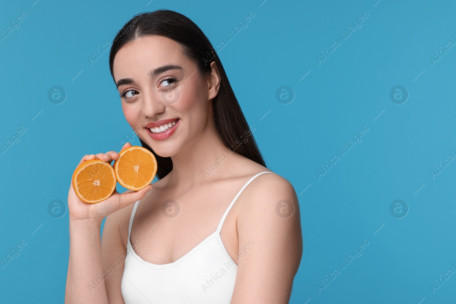 Photo of Beautiful young woman with pieces of orange on light blue background. Space for text