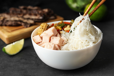 Photo of Chopsticks with tasty cooked rice noodles over bowl on black table