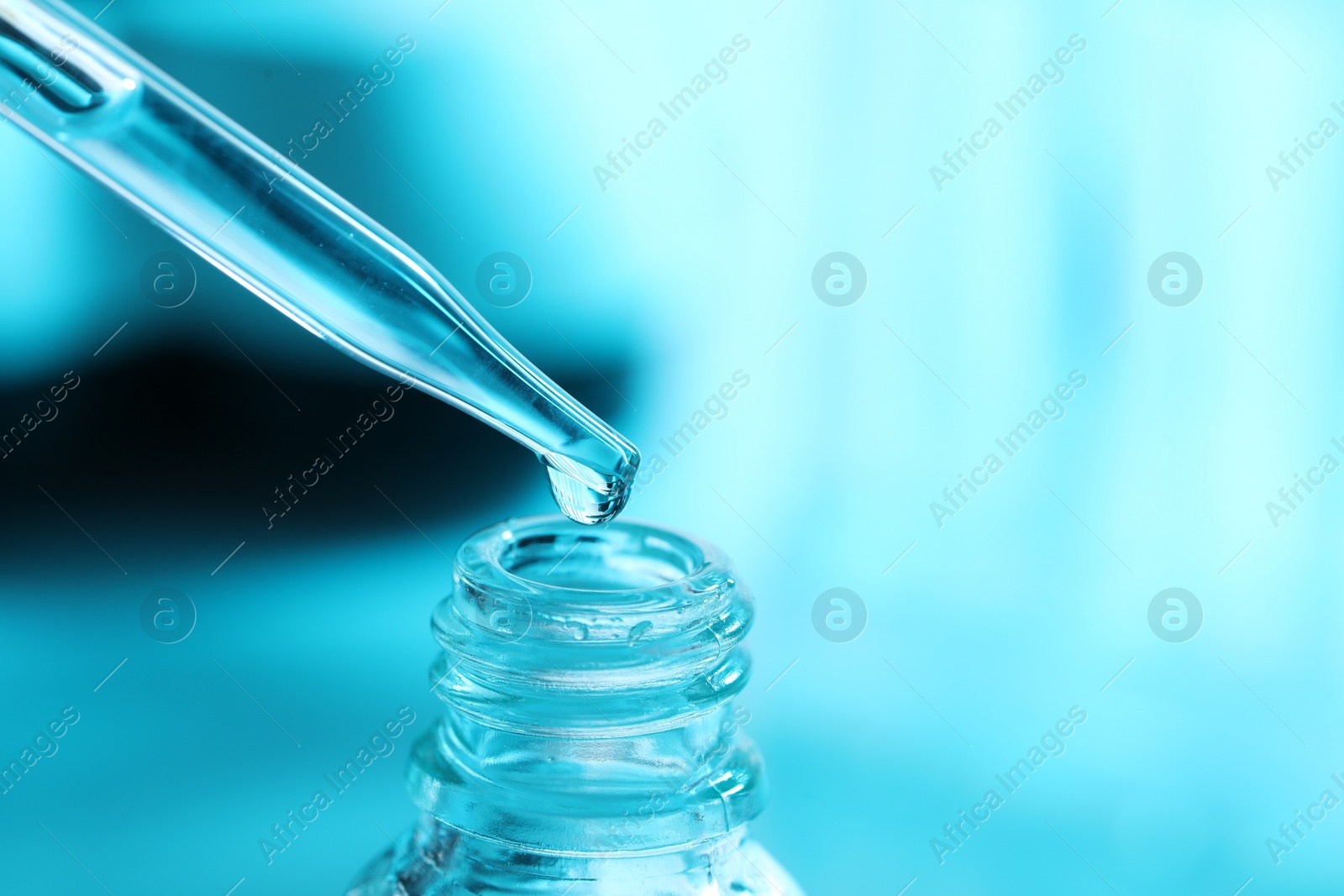 Photo of Dripping liquid from pipette into glass bottle on light blue background, closeup