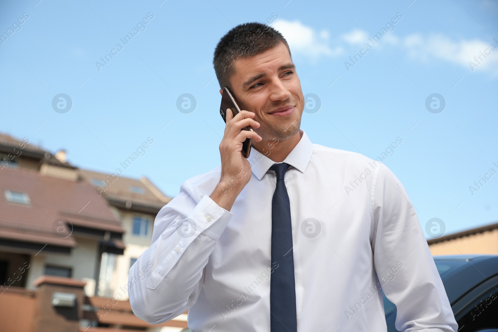 Photo of Attractive young man talking on phone near luxury car outdoors