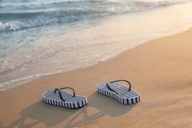 Striped beach slippers on sand near sea, space for text