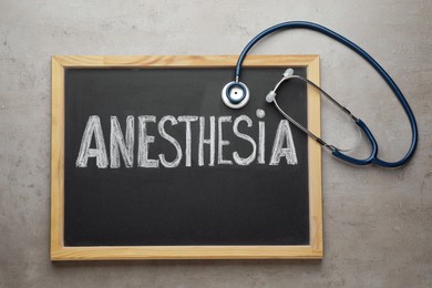 Photo of Blackboard with word Anesthesia and stethoscope on grey table, top view