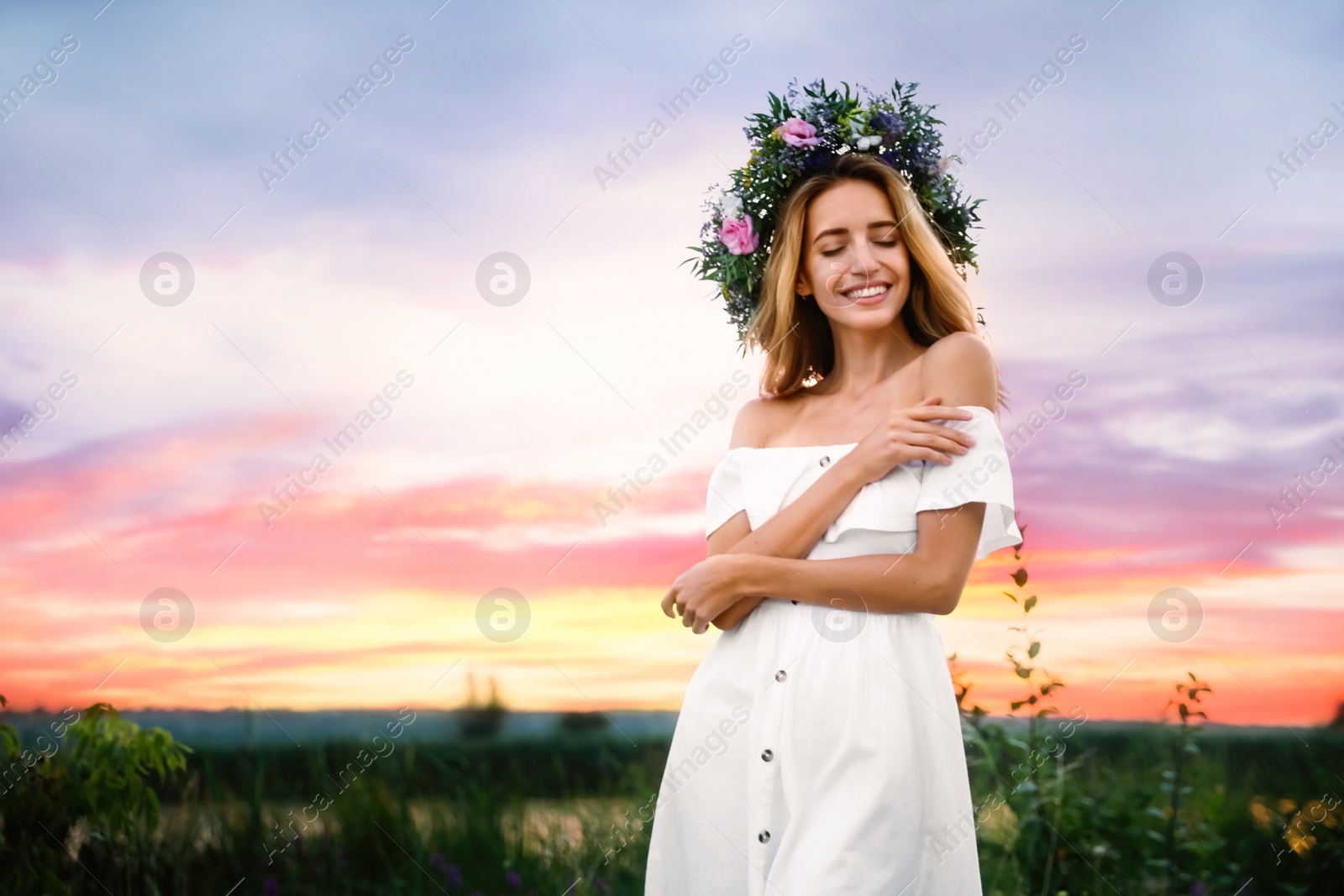 Photo of Young woman wearing wreath made of beautiful flowers outdoors at sunset