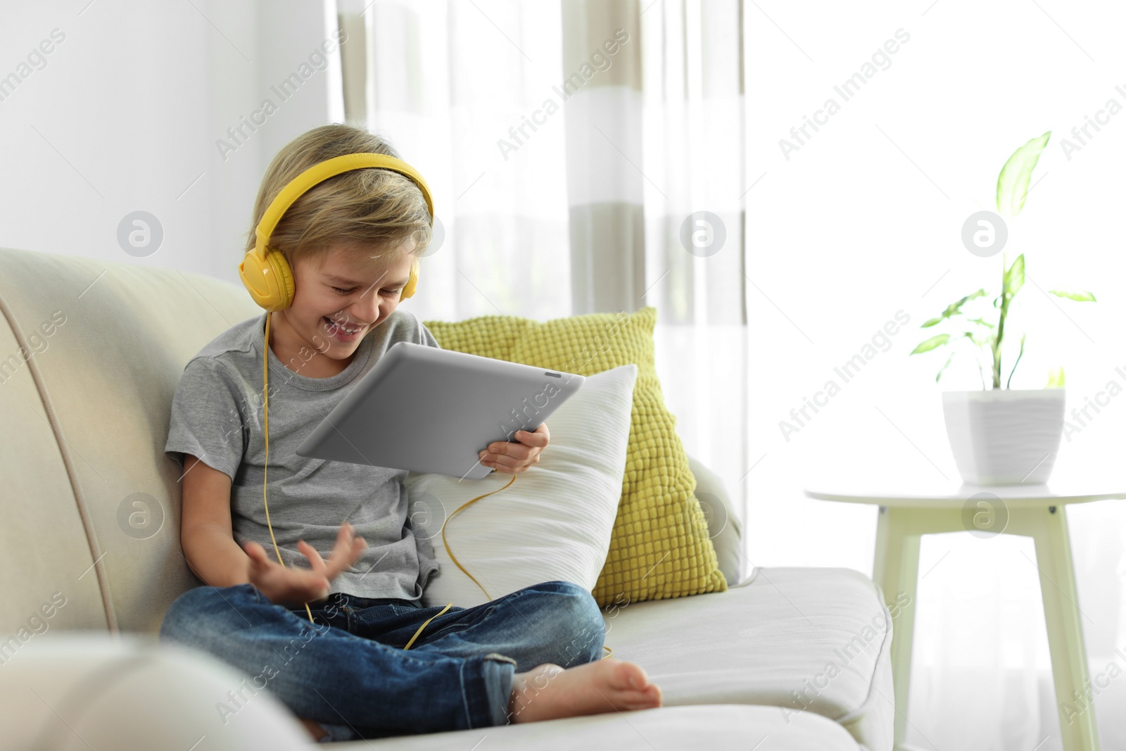 Photo of Cute little boy with headphones and tablet listening to audiobook at home