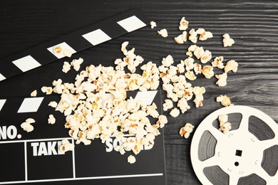 Tasty popcorn, film reel and clapperboard on wooden background, top view. Cinema snack