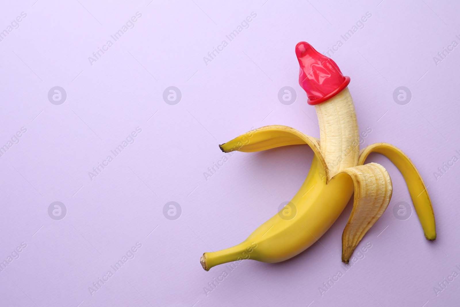 Photo of Banana with condom on lilac background, top view and space for text. Safe sex concept