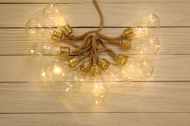 Photo of String lights with lamp bulbs on wooden background, top view