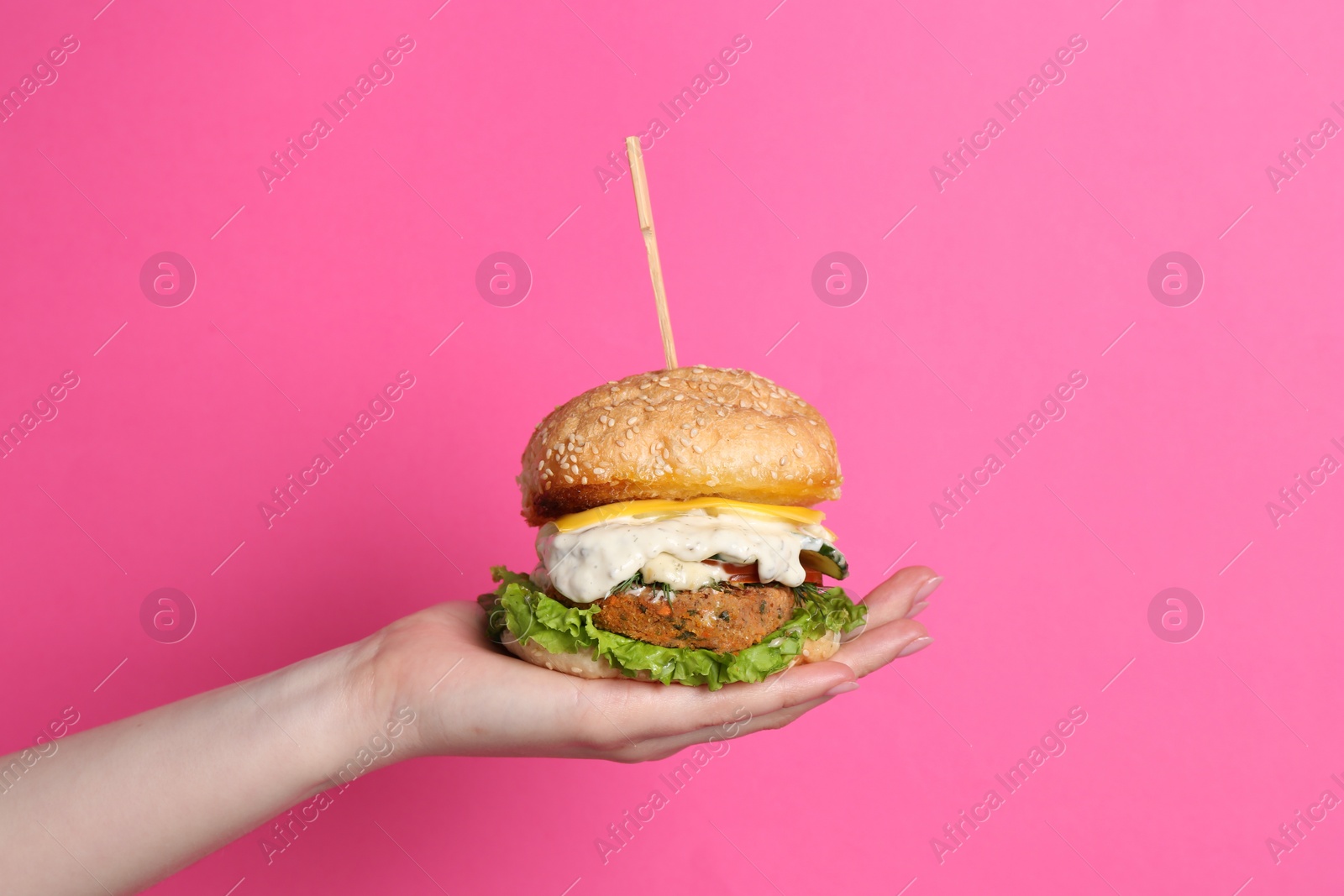 Photo of Woman holding delicious vegetarian burger on pink background, closeup