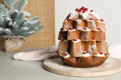 Photo of Delicious Pandoro Christmas tree cake with powdered sugar and berries near festive decor on grey table. Space for text