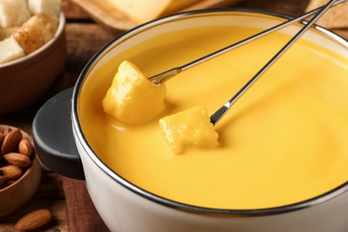 Photo of Pot of tasty cheese fondue and forks with bread pieces on table, closeup