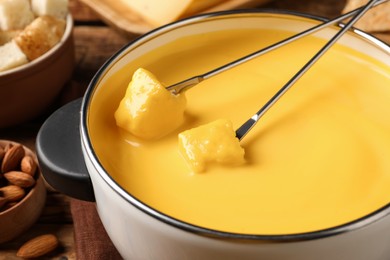 Pot of tasty cheese fondue and forks with bread pieces on table, closeup